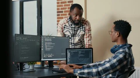 Software developer sitting at desk with multiple screens and laptop running code Stockfoto's