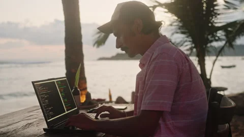 Software developer works on laptop at beach cafe, programming with sea view at Stock Footage 281238396