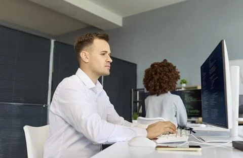 Software developers coding at computers in modern office with desktop monitors 스톡 사진