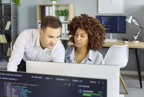 Software developers collaborating at monitors in modern office, reviewing code Photos