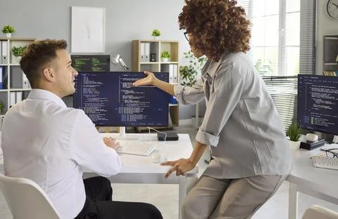 Software developers collaborating in office, reviewing code on dual monitors Stock Photos