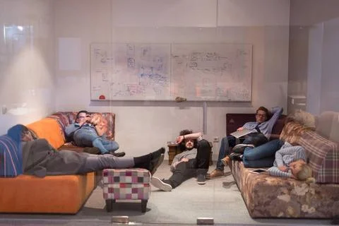Software developers sleeping on sofa in creative startup office group of y... Stock Photos