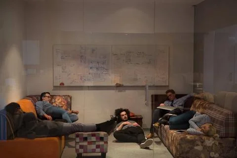 Software developers sleeping on sofa in creative startup office group of y... 스톡 사진