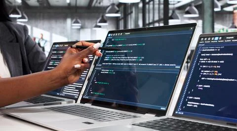 Software Engineer Carefully Reviews Code On Laptop At Busy Office Desk. Stockfoto's