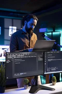 Software engineer checking code displayed on computer monitors in apartment Stockfoto's