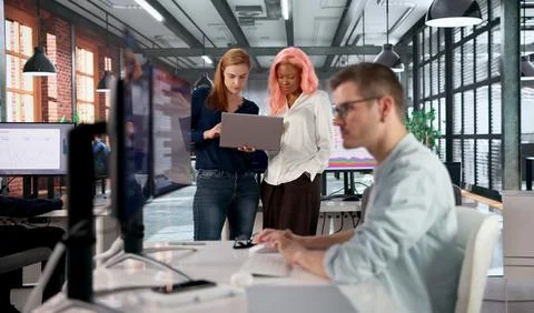 Software Engineer Discusses Code With Diverse Team In Busy Office Workspace. Stock Photos