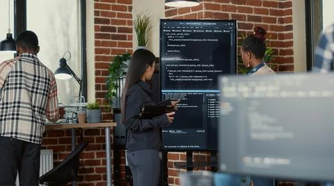 Software engineer holding digital tablet analyzing code on wall screen tv Stock Photos