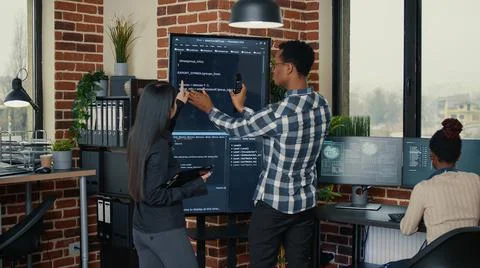 Software engineers analyzing code on wall screen tv comparing errors using Stock Photos