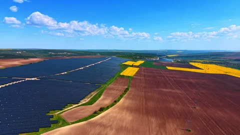 Solar arrays beside patchwork farmland and power lines, dark panels, tilled soil 動画素材 337912745