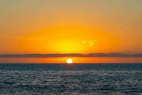 The solar disk beneath a long cloud over the ocean at sunset. Stock-Fotos