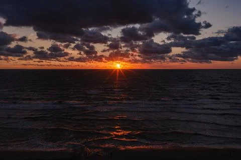 Solar eclipse covering the sun during sunset over ocean waters and clouds Stock Photos
