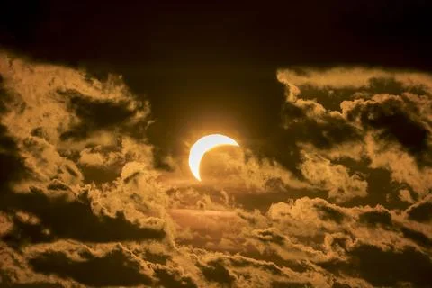 Solar eclipse with crescent sun covered by moon and clouds at sunset time. Stock Photos