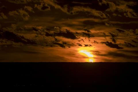 Solar eclipse during sunset with dark clouds covering the glowing sun. Stock Photos