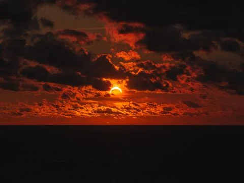 Solar eclipse during sunset with dark clouds over ocean horizon Stock Photos