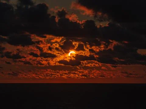 Solar eclipse during sunset with dark clouds over the dark ocean water Stock Photos