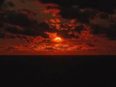 Solar eclipse during sunset with dark clouds over ocean horizon Stock-Fotos