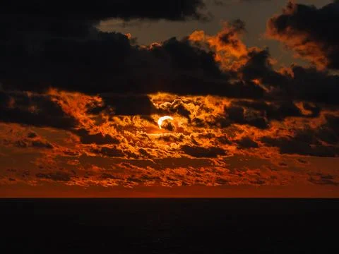 Solar eclipse during sunset over ocean with dark clouds and bright crescent s Stock Photos