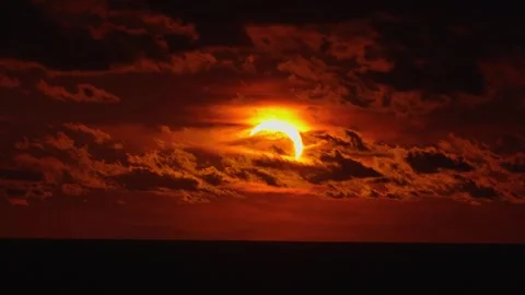 Solar eclipse occurs during sunset as clouds drift over ocean horizon. Vídeo Stock 342172683