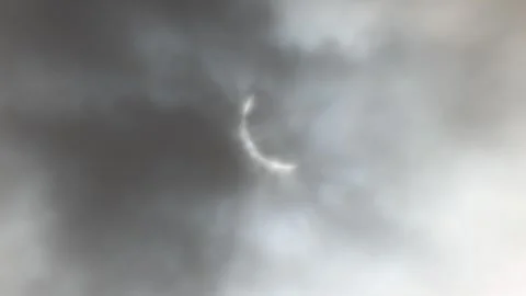 Solar Eclipse with partial totality is seen through dramatic gray cloudy ski Stock Footage 271303583