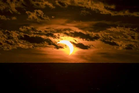 Solar eclipse partially covering the sun during sunset time with dark clouds. Stock Photos
