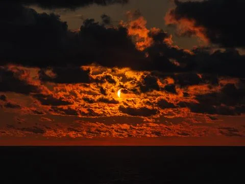 Solar eclipse partially covering the sun during sunset over sea water. Stock Photos