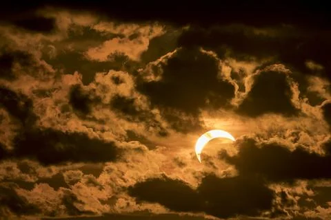 Solar eclipse partially covering the sun during sunset with dark clouds. Stock Photos
