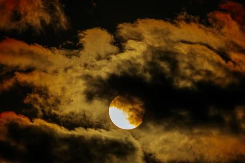 Solar eclipse partially obscured by dark clouds with vibrant orange and yel.. Stock Photos