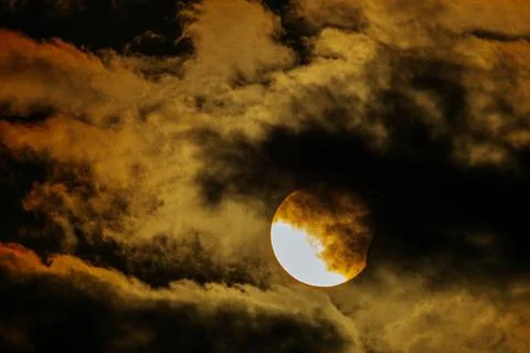Solar eclipse partially obscured by dark clouds, showcasing the sun's brigh.. Stock Photos