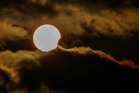 Solar eclipse partially obscured by dark clouds with a bright sun peeking t.. Stock Photos