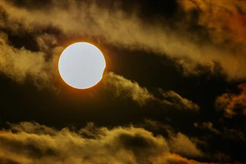 Solar eclipse with the sun partially obscured by clouds, showcasing a brigh.. Stock Photos