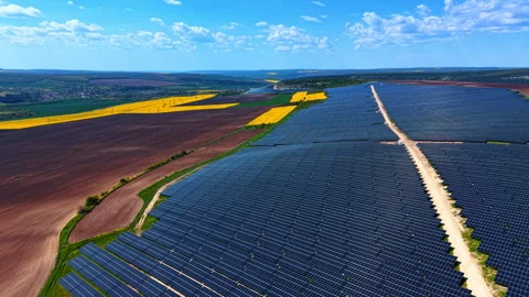 Solar farm bordering plowed fields and rapeseed. Dark panel rows meet brown Video stock 336899074