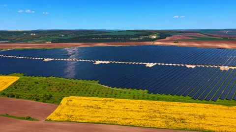 Solar farm framed by rapeseed and farmland. Dark arrays on green plateau with Vídeos de archivo 336899229