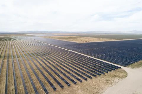 Solar farm with rows of panels on dry terrain under cloudy sky Stock Photos
