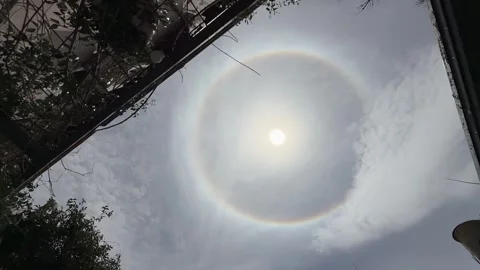 Solar halo forms a circular ring around sun in hazy sky framed by courtyard Stock Footage 348786031