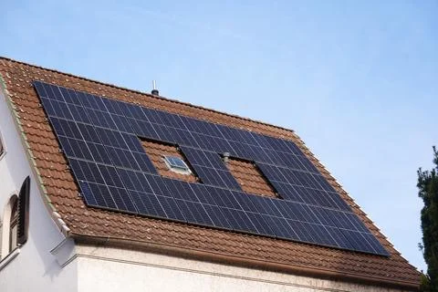 Solar panel array covers the roof of a residential building under a clear blue Stock Photos