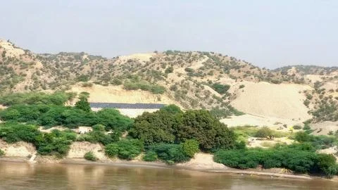 Solar Panel Array Installed On Arid Hillside Beside Muddy River Stock Photos