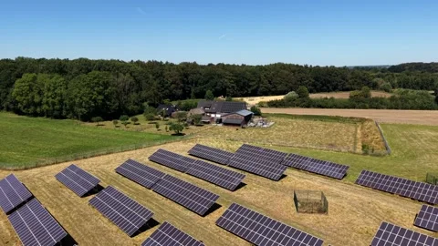 Solar panel array lines golden stubble field beside farmhouse and dense forest Stockbeeldmateriaal 341836874