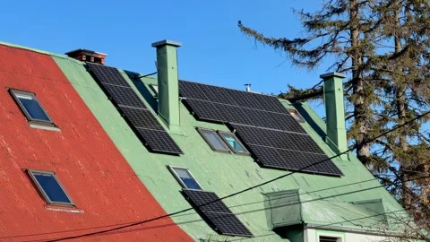 A solar panel array is mounted on the green pitched roof of a residential Vídeos de archivo 345822496
