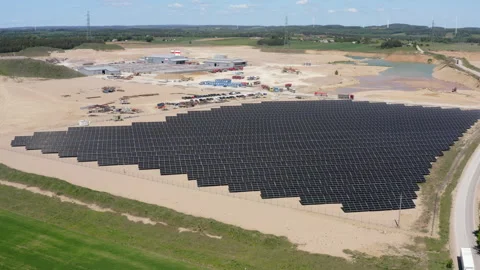 Solar Panel Array On Sandy Terrain Near Industrial Site. Wind Turbines In Stock Footage 310921571