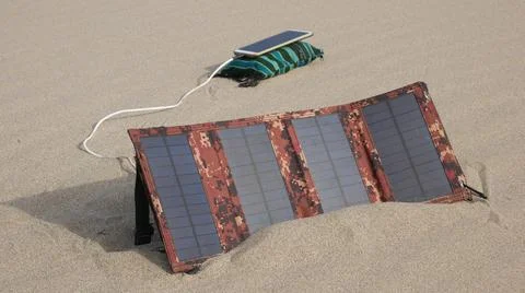 A solar panel charges a smartphone in a sandy desert 스톡 사진