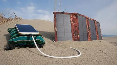 The solar panel charges the smartphone in the sandy desert against the backdr 스톡 사진