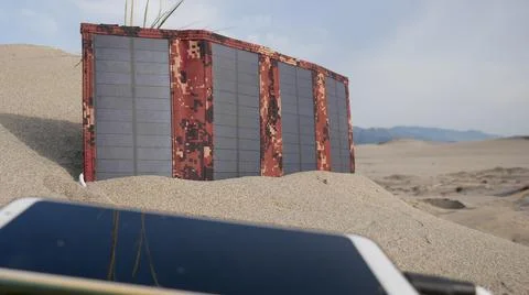 The solar panel charges the smartphone in the sandy desert against the backdr 스톡 사진