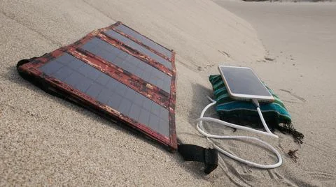 A solar panel charges a smartphone in a sandy desert 스톡 사진