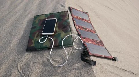 A solar panel charges a smartphone in a sandy desert 스톡 사진