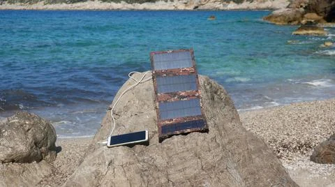 The solar panel charges the smartphone on the seashore 스톡 사진