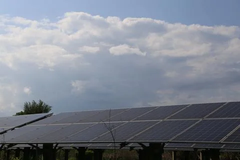 A solar panel farm under a cloudy sky, with one roof in the foreground and .. Stock Photos