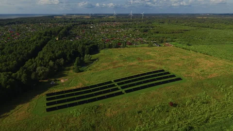 Solar panel field on grassy hillside near rural village, forest edge and wind Stock Footage 344661106