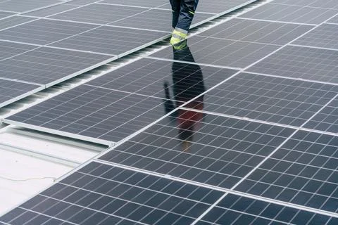 Solar panel installation on a rooftop with a technician working in daylight Stock Photos