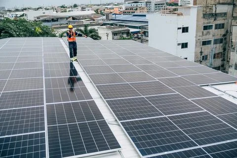 Solar panel installation on a rooftop by a worker during daylight in an urb.. Stock Photos