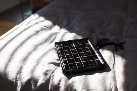 Solar panel is lying on bedding, blinds are casting striped shadows and cables Stock Photos